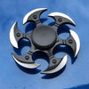 A black metal fidget spinner with a rainbow finish is shown against a blue background.