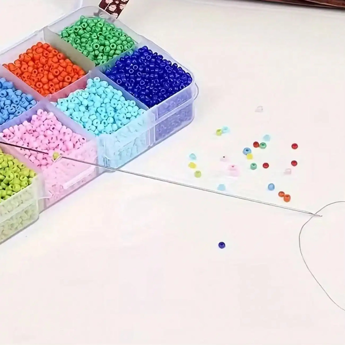 A collection of colorful metal beading needles and beads in various shades are displayed in clear plastic containers on a whi