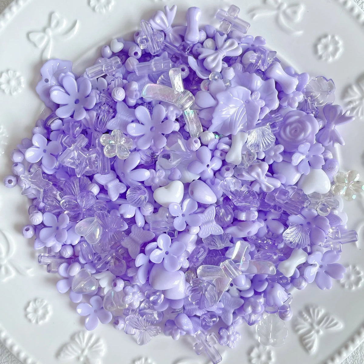 A pile of purple and white Y2K acrylic bow and flower beads for DIY jewelry making