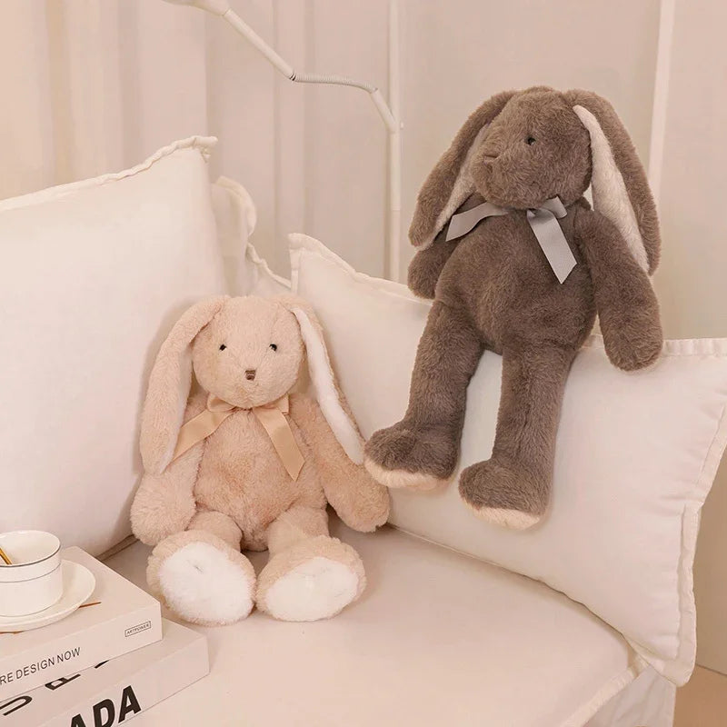 A soft gray bunny plush toy with long ears and a bow is resting on a white pillow.