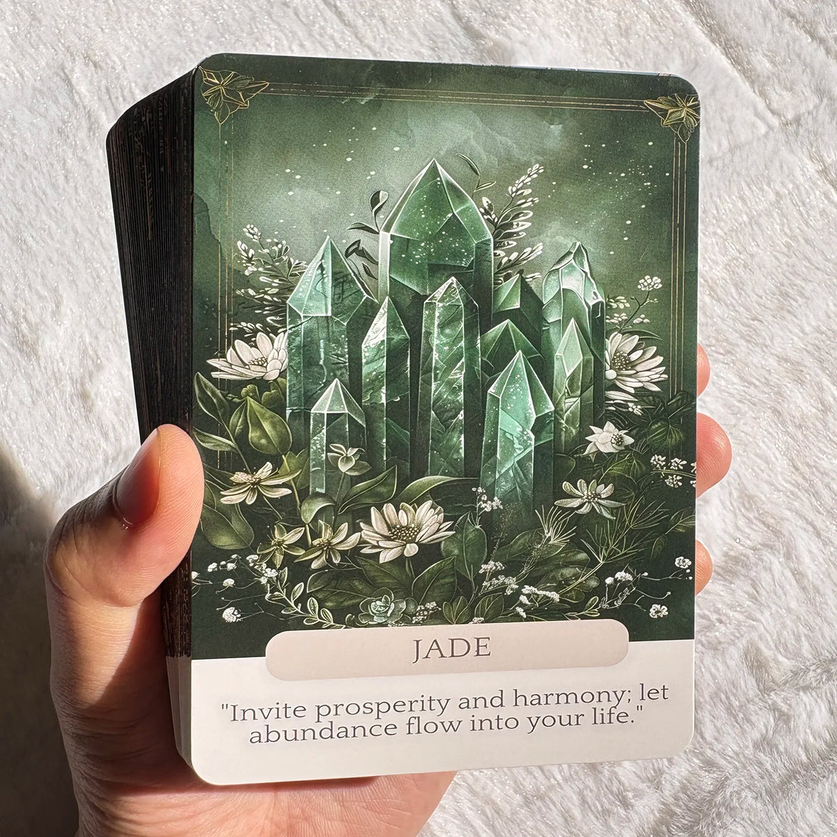 A Jade crystal oracle card featuring an emerald green geometric design surrounded by white flowers and foliage.