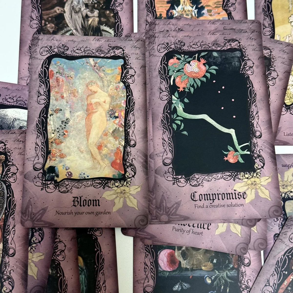 A stack of purple and black oracle cards featuring illustrations like Bloom and Compromise.