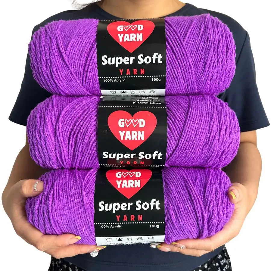 Three skeins of purple Super Soft Yarn labeled GOVD YARN are held against a dark shirt.