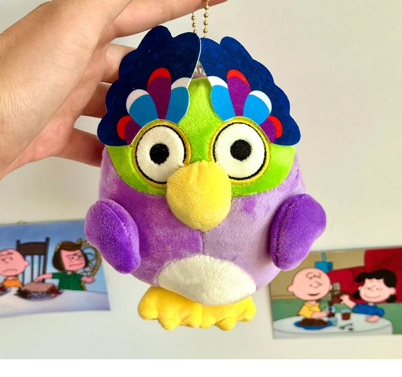 A purple and green plush toy of an owl with blue feathers and large eyes being held by a hand.