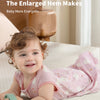 A smiling baby wearing a pink sleeveless sleeping bag on a light-colored surface.