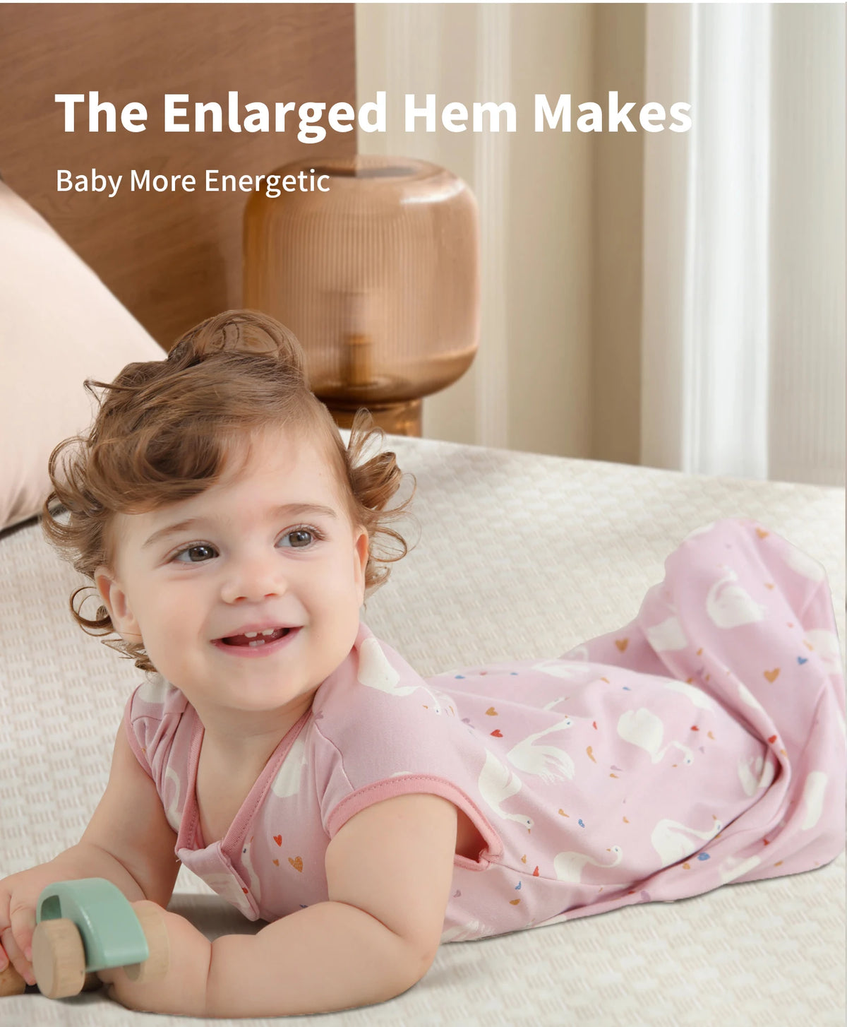 A smiling baby wearing a pink sleeveless sleeping bag on a light-colored surface.
