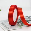 A roll of red satin ribbon used for gift wrapping or crafts, lying next to a piece of paper.