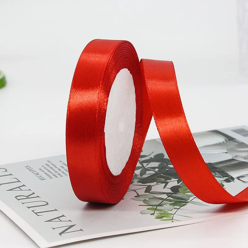 A roll of red satin ribbon used for gift wrapping or crafts, lying next to a piece of paper.