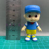 A playful cartoon PVC figurine of a boy wearing a blue cap and shirt, standing next to a ruler.