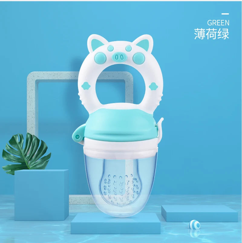 A white silicone baby food feeder with a teal lid and a green teether is displayed on a light blue background.