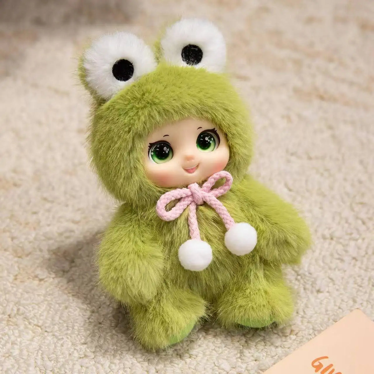 A soft green plush pendant shaped like a cute, fuzzy animal face with large eyes and a pink bow.