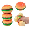 A bright orange squishy hamburger stress ball with a green top and bottom bun is being held by a hand.