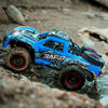 A blue RC monster truck driving through water and mud on a rocky terrain.