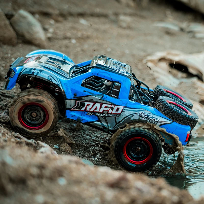 A blue RC monster truck driving through water and mud on a rocky terrain.