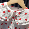 White long-sleeve shirt for a baby girl with a red strawberry print, displayed on a wooden hanger.