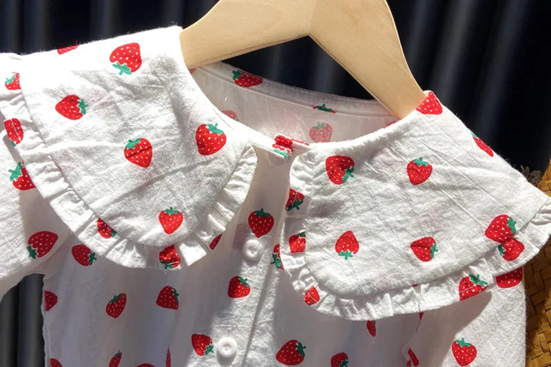 White long-sleeve shirt for a baby girl with a red strawberry print, displayed on a wooden hanger.