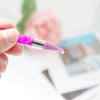 A hand holds a purple double-head diamond painting pen with a wax tip against a blurred background.