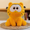 A fluffy orange Garfield plush doll with large eyes and pink nose sitting on a woven mat.