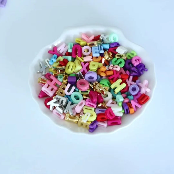 A pile of mixed acrylic letter beads in various colors and shapes on a white dish.
