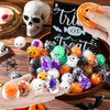 A hand holds a bowl filled with five Halloween squeeze stress balls featuring skulls, bats, and orange colors.