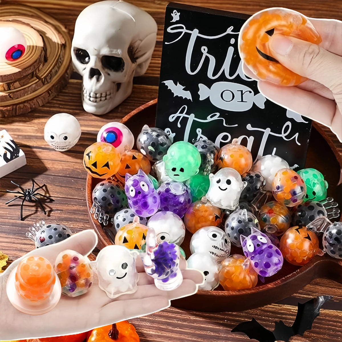 A hand holds a bowl filled with five Halloween squeeze stress balls featuring skulls, bats, and orange colors.