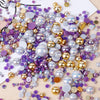 A scattered collection of mixed resin rhinestone pearls with an AB finish in various shades of purple, silver, and gold.