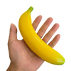 A hand is holding a bright yellow squishy banana stress relief toy.