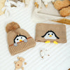 A knitted penguin hat and scarf set featuring black and white designs on a beige background