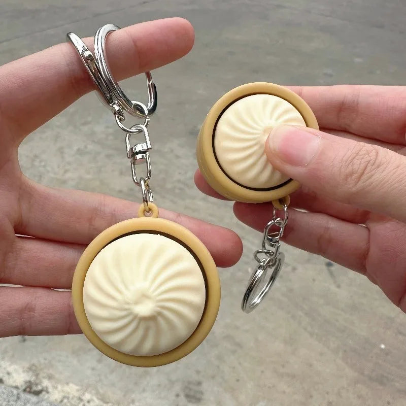 A hand holds a keychain featuring a round, light yellow silicone fidget toy shaped like a steamed bun.