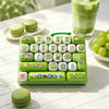 A green keyboard keycap clicker featuring various cute, themed keycaps and a lime green plastic base, next to macarons and a 
