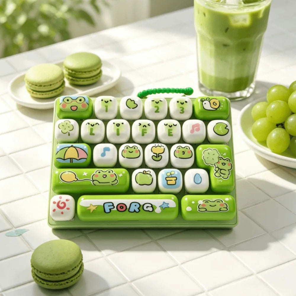 A green keyboard keycap clicker featuring various cute, themed keycaps and a lime green plastic base, next to macarons and a 
