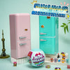 A pink miniature fridge playset with a teal refrigerator and a small food capsule on a white shelf.