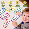 A young boy is smiling while looking at various phonics flip books and sight word flash cards laid out on a white table.