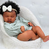 A newborn baby with dark curly hair wearing a green and white checkered outfit is resting in a white knitted basket.
