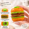 An orange burger-shaped stress relief toy with layered components is held in a hand.