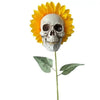 A decorative stake featuring a skull carved into the center of a bright yellow sunflower head with green leaves.