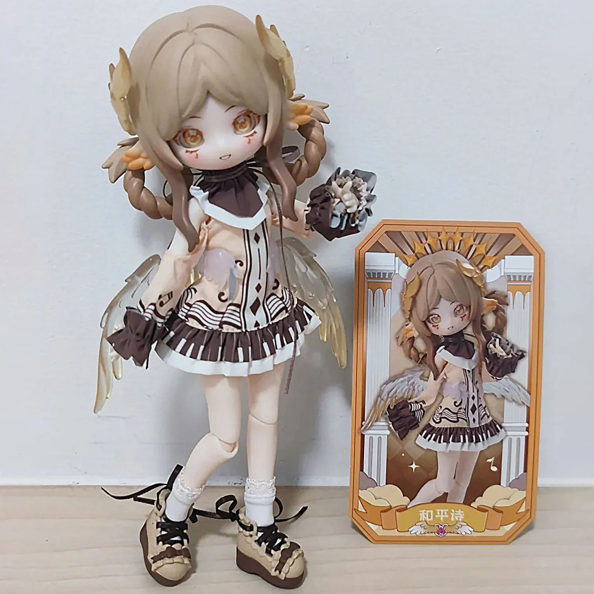 A detailed anime-style Ball-Jointed Doll with light brown hair and feathered wings standing next to its packaging box.