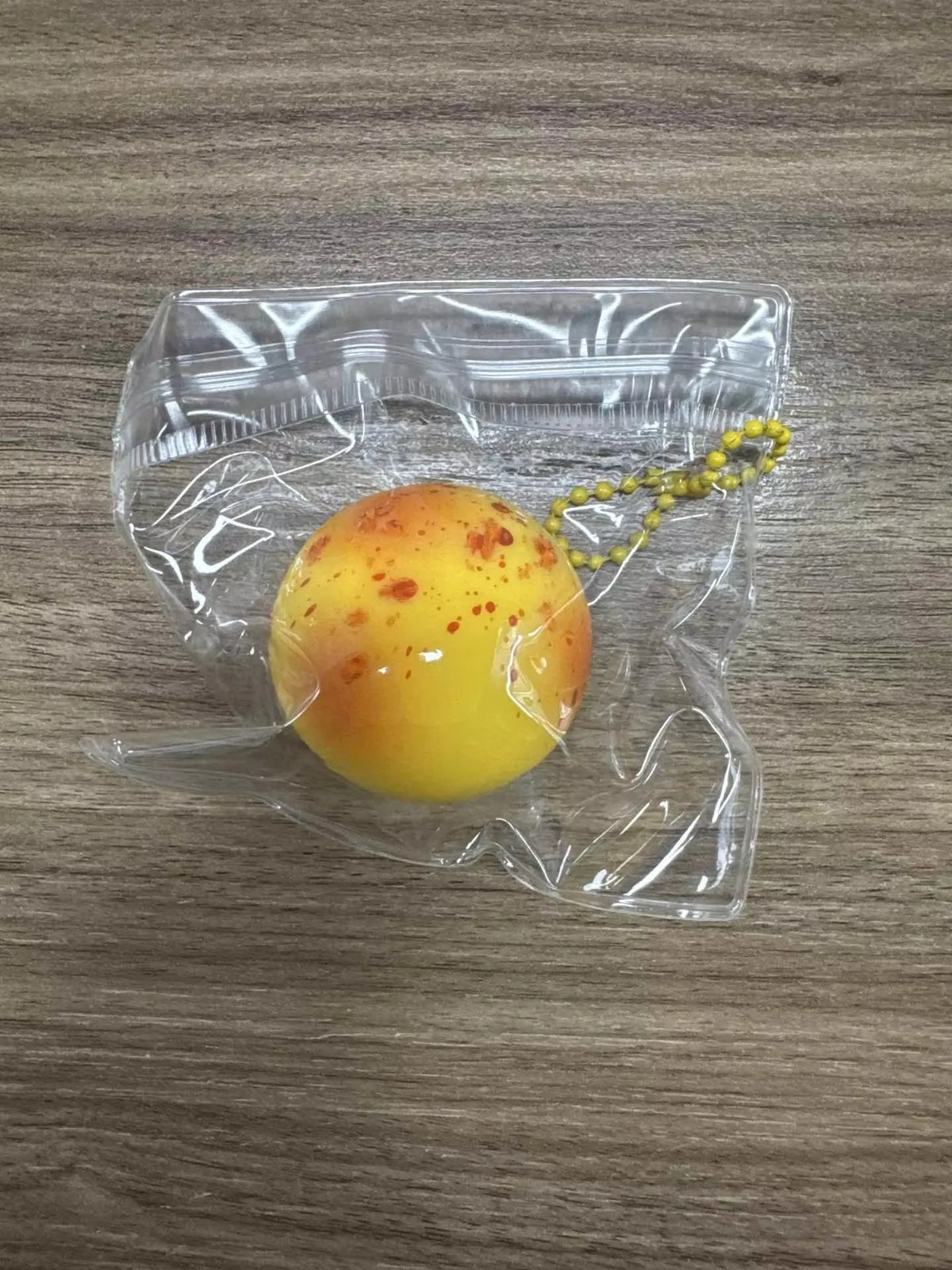 A yellow squishy potato fidget toy is visible inside a clear plastic bag on a wooden surface.