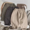 A pair of beige loose wide-leg harem pants for boys lying on a light surface.
