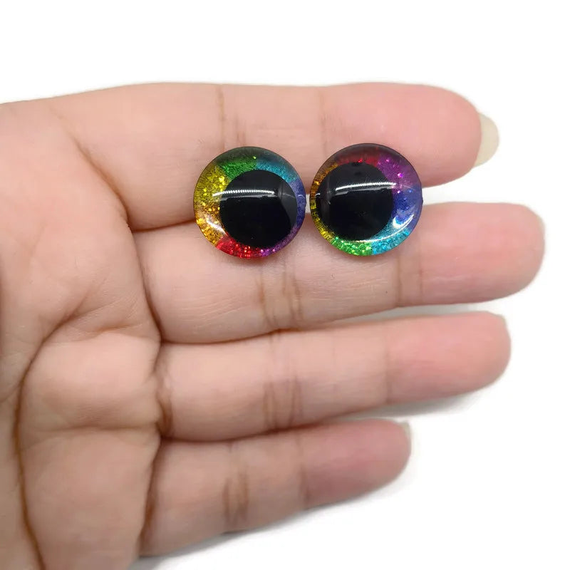Pair of glitter cartoon safety eyes with iridescent colors displayed on a hand.