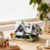 A miniature wooden building set depicting a cabin and windmill scene on a light wooden surface.