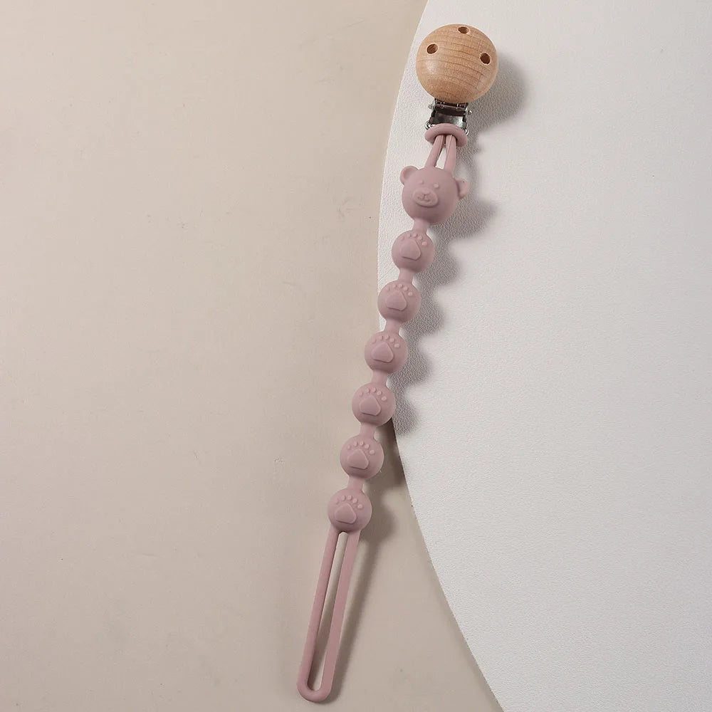 A silicone pacifier clip featuring a wooden bear paw and pink silicone beads on a thin pink cord.