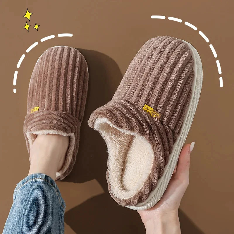 A pair of brown faux fur slippers being held, showing the plush interior and exterior texture.