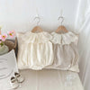 A beige baby girl sleeveless jumpsuit with a lace collar displayed on a white bed with natural light.