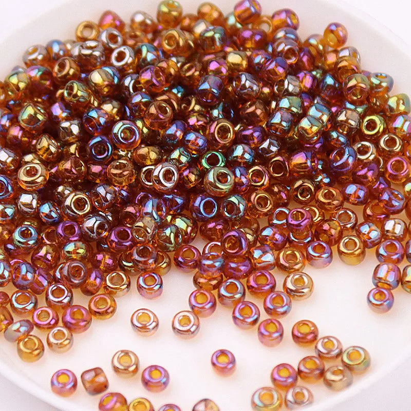 A pile of multi-sized magic color glass rice beads in shades of amber, purple, and gold.