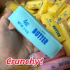 A hand holds a light blue butter stick squishy stress ball with yellow packaging in the background.