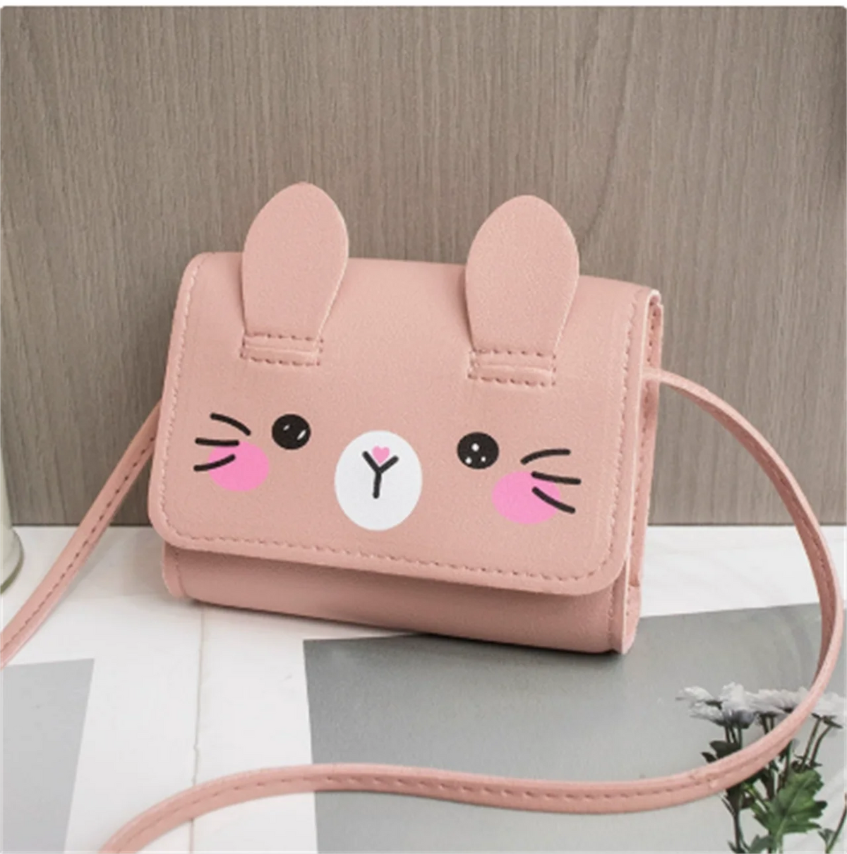 A pink cat-face mini PU leather crossbody handbag with long ears and whiskers resting on a gray surface.