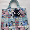 A patterned fabric tote bag featuring a cute black cat design on a light blue and pink background.
