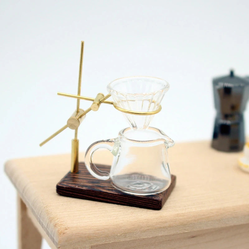 A miniature hand-brewed coffee stand set for dollhouse featuring a glass teapot and a brass-tipped stirrer.