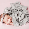 A newborn baby sleeping peacefully wrapped in a gray knit wrap with a pearl headband.